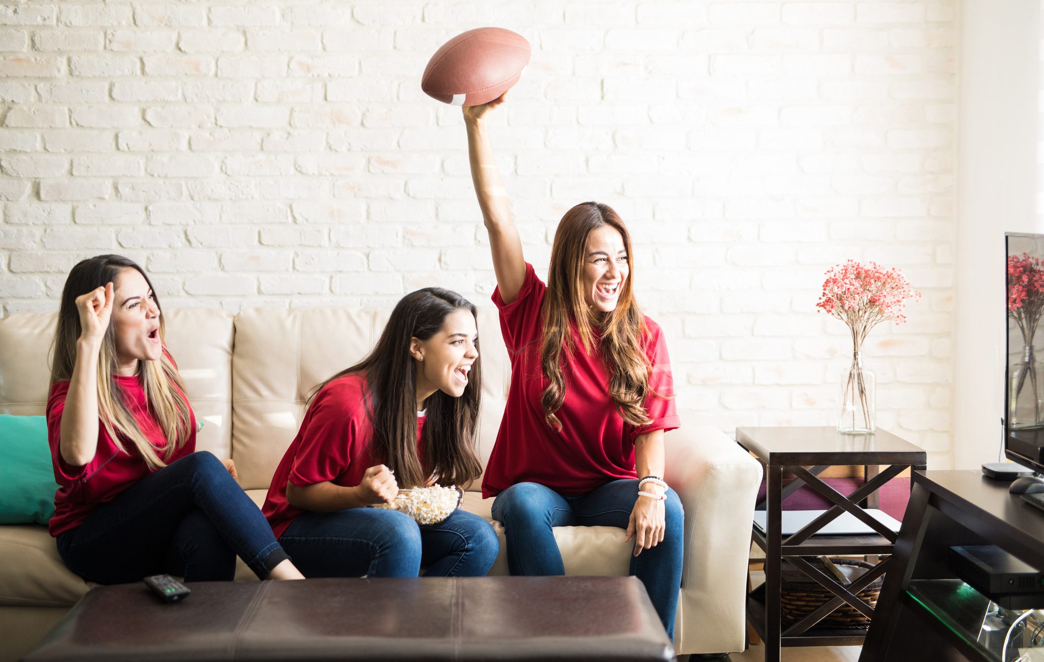 Three roomies wearing team jerseys and watching a football team on tv, celebrating a touchdown